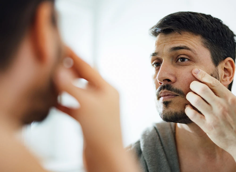 Man touching face in mirror | Ottawa Plastic Surgery in Ottawa, Canada