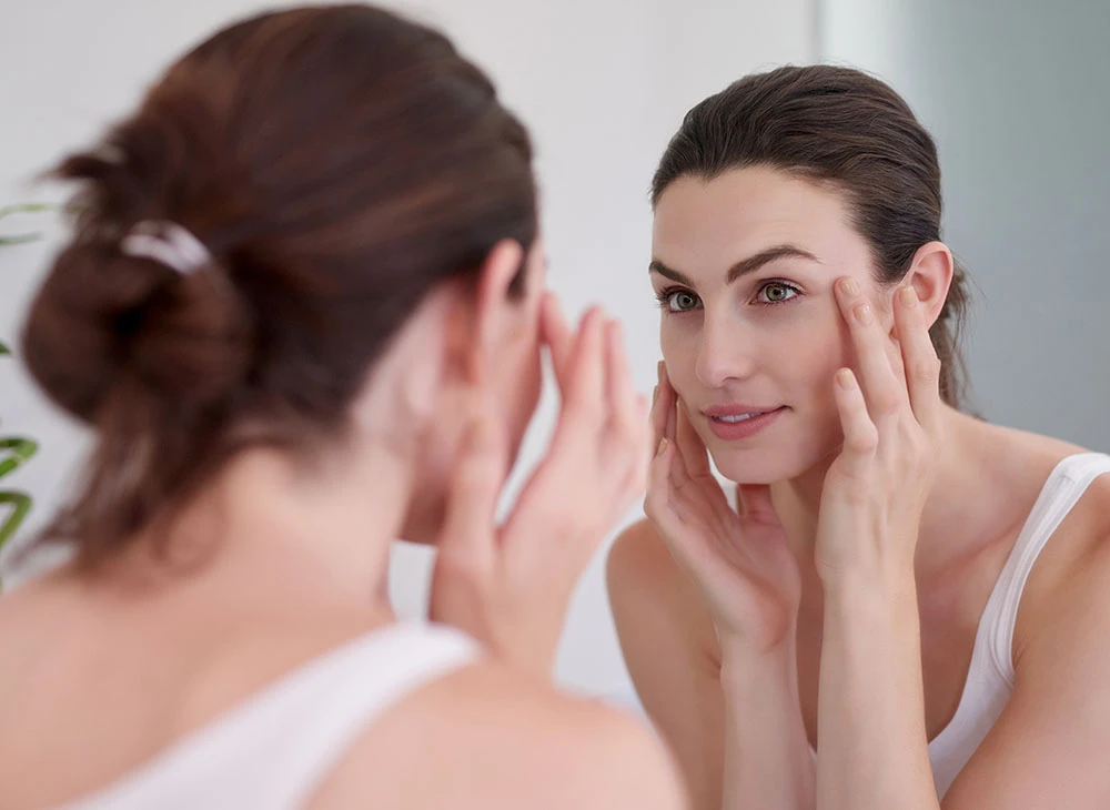 woman touching face in mirror | Ottawa Plastic Surgery in Ottawa, Canada